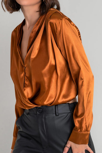 Blusa corta satinada de escote v cruzado con plisados decorativos en hombros, manga larga con puño abotonado y rib elástico en bajo.