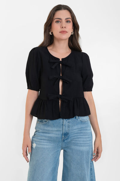 Blusa de manga corta abullonada con rib elástico en bordes, cuello redondo y cierre frontal con lazos amarrables. Detalle de peplum con olanes en bajo.