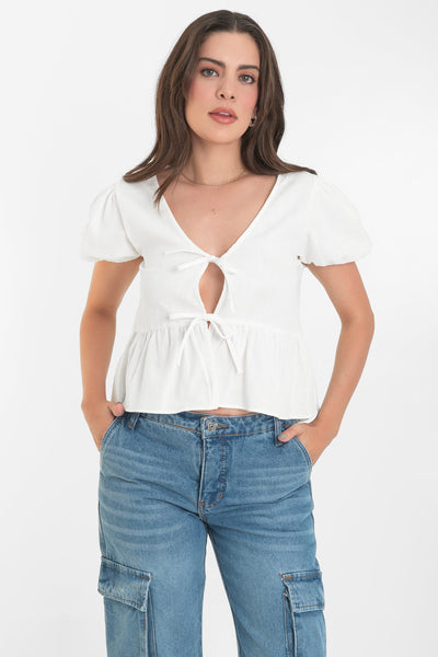 Blusa de manga corta abullonada con rib elástico en bordes, escote v y cierre frontal con lazos amarrables. Detalle de peplum con olanes en bajo.