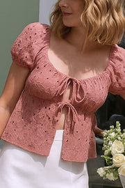 Blusa corta eyelet de manga corta abullonada, rib elástico en cintura, escote redondo con plisados y cierre frontal con lazos amarrables. Detalle de perforado en tejido bordado.