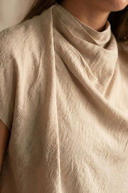 Blusa fluida de manga corta seguida, cuello mock seguido con plisados decorativos en hombro y cuello. Cierre posterior con botones y ojales.