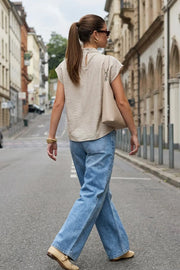 Blusa fluida de manga corta seguida, cuello mock seguido con plisados decorativos en hombro y cuello. Cierre posterior con botones y ojales.