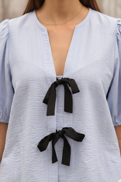 Blusa de fit fluido, estampado rayas, manga corta abullonada con rib elástico en bordes, cuello redondo y escote v. Cierre frontal con doble lazo amarrable en contraste y pinza amplitud en espalda.