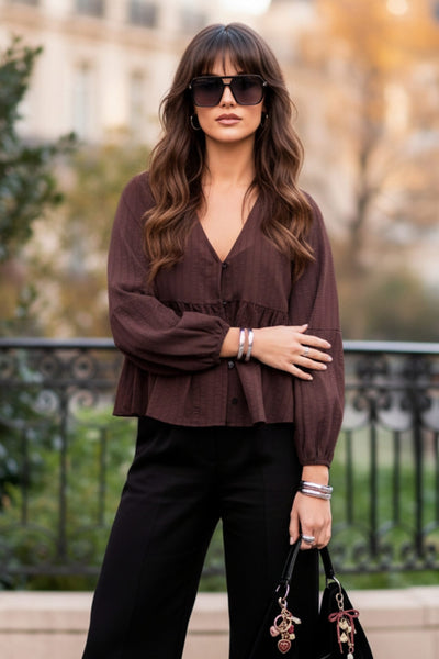 Blusa de fit fluido, manga larga abullonada con rib elástico en puños, escote v, plisados decorativos en hombros y peplum con olanes en bajo. Cierre frontal con hilera de botones.