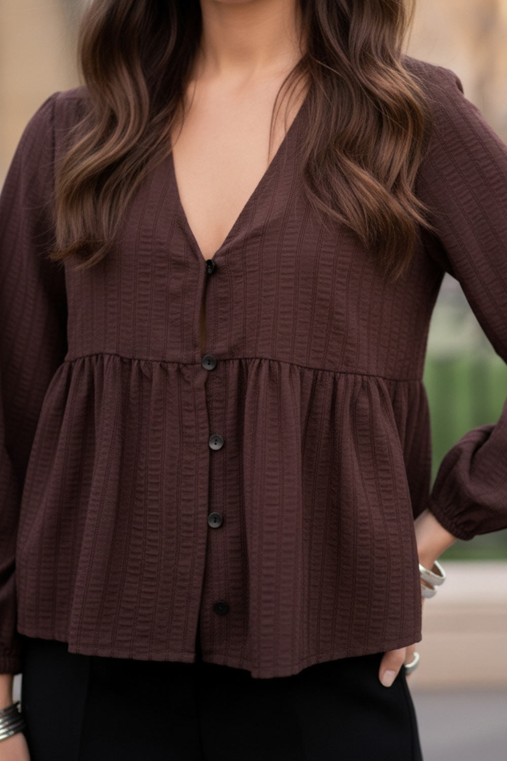 Blusa de fit fluido, manga larga abullonada con rib elástico en puños, escote v, plisados decorativos en hombros y peplum con olanes en bajo. Cierre frontal con hilera de botones.