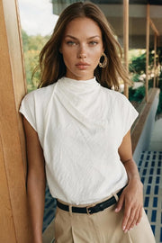 Blusa fluida de manga corta seguida, cuello mock seguido con plisados decorativos en hombro y cuello. Cierre posterior con botones y ojales.