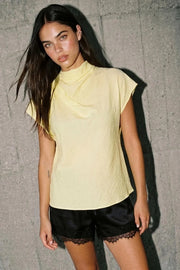 Blusa fluida de manga corta seguida, cuello mock seguido con plisados decorativos en hombro y cuello. Cierre posterior con botones y ojales.