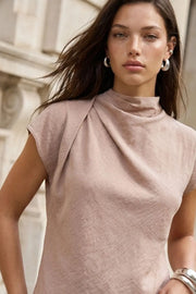 Blusa fluida de manga corta seguida, cuello mock seguido con plisados decorativos en hombro y cuello. Cierre posterior con botones y ojales.