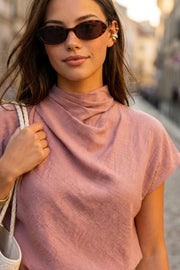 Blusa fluida de manga corta seguida, cuello mock seguido con plisados decorativos en hombro y cuello. Cierre posterior con botones y ojales.