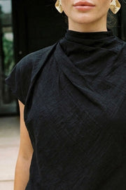 Blusa fluida de manga corta seguida, cuello mock seguido con plisados decorativos en hombro y cuello. Cierre posterior con botones y ojales.