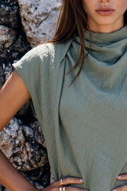 Blusa fluida de manga corta seguida, cuello mock seguido con plisados decorativos en hombro y cuello. Cierre posterior con botones y ojales.