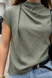 Blusa fluida de manga corta seguida, cuello mock seguido con plisados decorativos en hombro y cuello. Cierre posterior con botones y ojales.