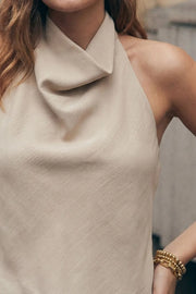 Blusa corta de fit fluido, sin mangas, cuello halter fluido con plisados, escote en espalda y lazo amarrable posterior. Cierre posterior con botón y ojal.