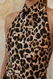 Blusa corta de fit fluido, sin mangas, estampado animal, cuello halter fluido con plisados, escote en espalda y lazo amarrable posterior. Cierre posterior con botón y ojal.