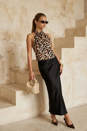 Blusa corta de fit fluido, sin mangas, estampado animal, cuello halter fluido con plisados, escote en espalda y lazo amarrable posterior. Cierre posterior con botón y ojal.