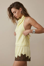 Blusa corta de fit fluido, sin mangas, cuello halter fluido con plisados, escote en espalda y lazo amarrable posterior. Cierre posterior con botón y ojal.