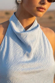 Blusa corta de fit fluido, sin mangas, cuello halter fluido con plisados, escote en espalda y lazo amarrable posterior. Cierre posterior con botón y ojal.