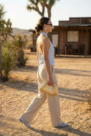 Blusa corta de fit fluido, sin mangas, cuello halter fluido con plisados, escote en espalda y lazo amarrable posterior. Cierre posterior con botón y ojal.