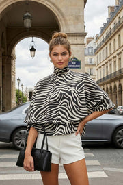 Blusa corta tipo capa de cuello alto con plisados, capas de olanes, estampado animal y escote en espalda con lazo amarrable posterior.