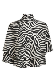 Blusa corta tipo capa de cuello alto con plisados, capas de olanes, estampado animal y escote en espalda con lazo amarrable posterior.