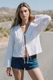 Blusa corta de fit fluido, manga larga con puño amplio, escote v con solapa y cierre frontal con lazos amarrables.