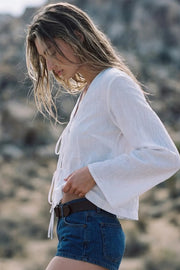 Blusa corta de fit fluido, manga larga con puño amplio, escote v con solapa y cierre frontal con lazos amarrables.