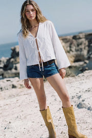 Blusa corta de fit fluido, manga larga con puño amplio, escote v con solapa y cierre frontal con lazos amarrables.