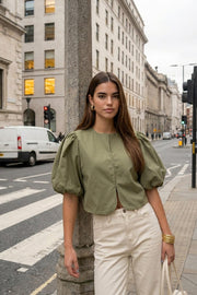 Blusa corta de fit recto, cuello redondo, manga corta amplia globo con volumen en borde, cierre frontal con broches ocultos y bajo curveado frontal.