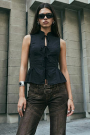 Blusa corta de fit ajustado, cuello mao, sin mangas y cierre frontal con lazos amarrables. Detalle de peplum con plisados y olanes en bajo.