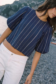 Blusa de estampado rayas, cuello redondo, manga corta abullonada, fit fluido y pinza de amplitud en espalda. Cierre posterior con botón y ojal.