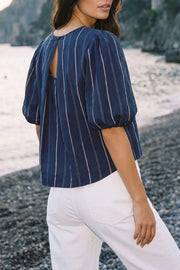 Blusa de estampado rayas, cuello redondo, manga corta abullonada, fit fluido y pinza de amplitud en espalda. Cierre posterior con botón y ojal.