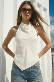 Blusa asimétrica de fit fluido, sin mangas, cuello halter fluido con plisados, escote en espalda y lazo amarrable posterior. Cierre posterior con botón y ojal. Detalle de bajo frontal asimétrico.