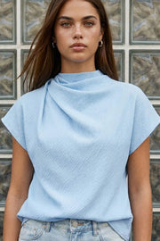 Blusa de cuello alto fluido, plisados en hombros, manga corta seguida y fit recto. Cierre posterior con botón y ojal.