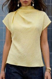 Blusa de cuello alto fluido, plisados en hombros, manga corta seguida y fit recto. Cierre posterior con botón y ojal.