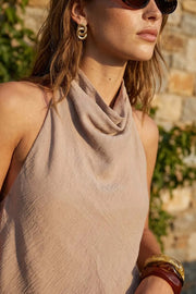Blusa asimétrica de fit fluido, sin mangas, cuello halter fluido con plisados, escote en espalda y lazo amarrable posterior. Cierre posterior con botón y ojal. Detalle de bajo frontal asimétrico.