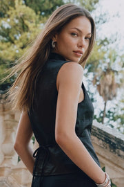 Blusa corta satinada de fit ajustado, sin mangas, cuello mao, pinzas frontales, cierre frontal con botones y abertura frontal con bajo curveado. Detalle de lazo amarrable posterior.
