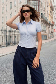 Camisa corta de estampado rayas, fit recto, manga corta abullonada con rib elástico en bordes, cuello camisero, cortes y plisados frontales. Cierre frontal con hilera de botones.