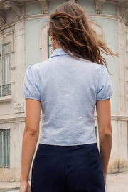 Camisa corta de estampado rayas, fit recto, manga corta abullonada con rib elástico en bordes, cuello camisero, cortes y plisados frontales. Cierre frontal con hilera de botones.