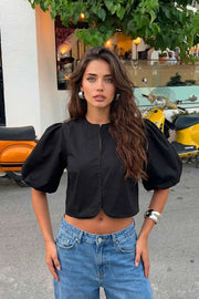 Blusa corta de fit recto, cuello redondo, manga corta amplia globo con volumen en borde, cierre frontal con broches ocultos y bajo curveado frontal.