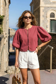 Blusa corta de fit recto, cuello redondo, manga corta amplia globo con volumen en borde, cierre frontal con broches ocultos y bajo curveado frontal.