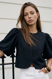 Blusa corta de fit recto, cuello redondo, manga corta amplia globo con volumen en borde, cierre frontal con broches ocultos y bajo curveado frontal.