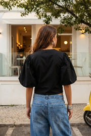 Blusa corta de fit recto, cuello redondo, manga corta amplia globo con volumen en borde, cierre frontal con broches ocultos y bajo curveado frontal.