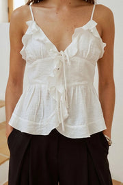 Blusa corta de tirantes delgados ajustables, escote v con olanes en borde, cortes frontales con plisados, peplum con olanes en bajo y cierre frontal con lazos amarrables.