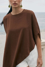 Blusa tipo túnica asimétrica, de cuello redondo, con hombreras, manga corta seguida, fit fluido y bajo asimétrico. Cierre posterior con cremallera oculta.