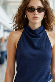 Blusa asimétrica de fit fluido, sin mangas, cuello halter fluido con plisados, escote en espalda y bajo frontal asimétrico. Detalle de textura en tejido, cierre posterior con botón y ojal.