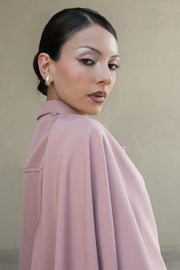 Camisa corta de fit fluido, manga larga amplia con puño abotonado, cuello camisero, detalle decorativo cruzado con plisados y olanes. Cierre frontal con hilera de botones en contraste. Detalle de pinza de amplitud en espalda.