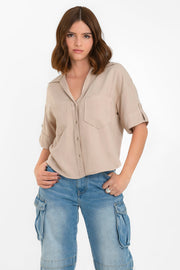 Camisa corta de fit recto, manga corta con doblez en borde y trabillas decorativas laterales, bolsillos frontales de parche, cuello camisero, bajo curveado y pinza de amplitud en espalda. Cierre frontal con hilera de botones en contraste