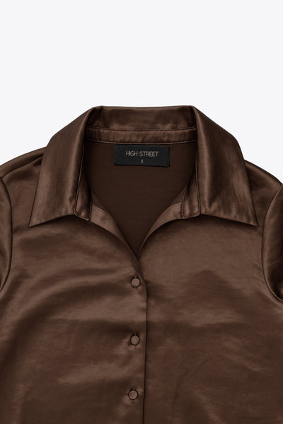 Camisa corta satinada de fit recto, cuello camisero, manga larga con puño abotonado, pinza de amplitud en espalda y cierre frontal con hilera de botones.