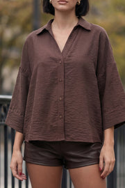 Camisa de fit oversized, manga 3/4 amplia con doblez en puños, cuello camisero, escote v, pinza de amplitud en espalda con trabilla decorativa y bajo curveado. Cierre frontal con hilera de botones en contraste.