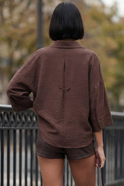 Camisa de fit oversized, manga 3/4 amplia con doblez en puños, cuello camisero, escote v, pinza de amplitud en espalda con trabilla decorativa y bajo curveado. Cierre frontal con hilera de botones en contraste.